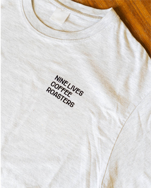 Grey t-shirt with 'Nine Lives Coffee Roasters' text on a wooden surface